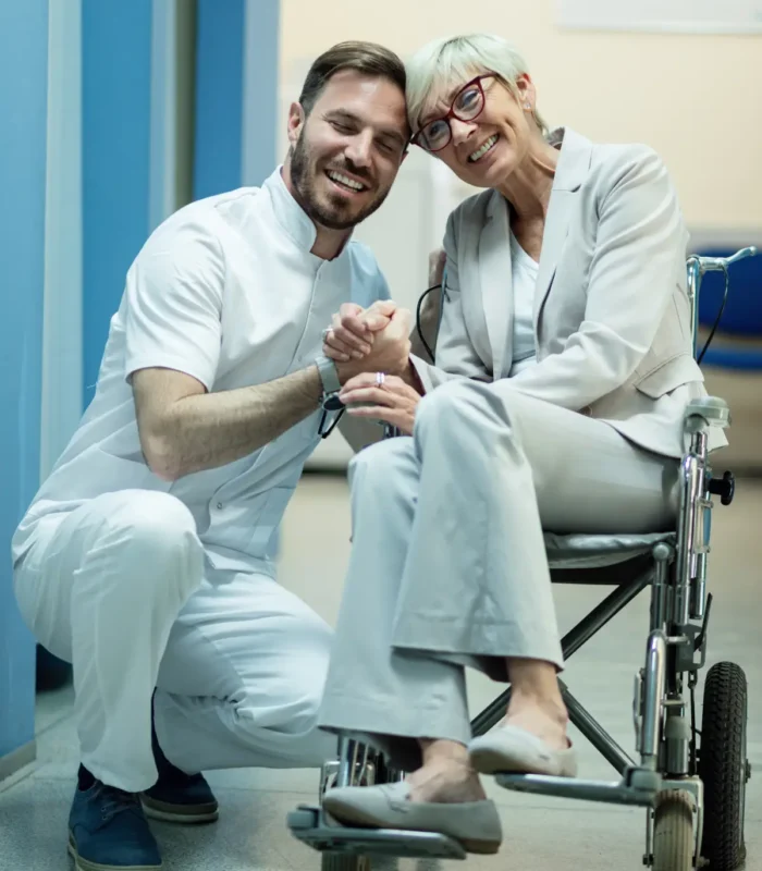 happy-mature-woman-wheelchair-holding-hands-with-her-doctor-hospital-hallway